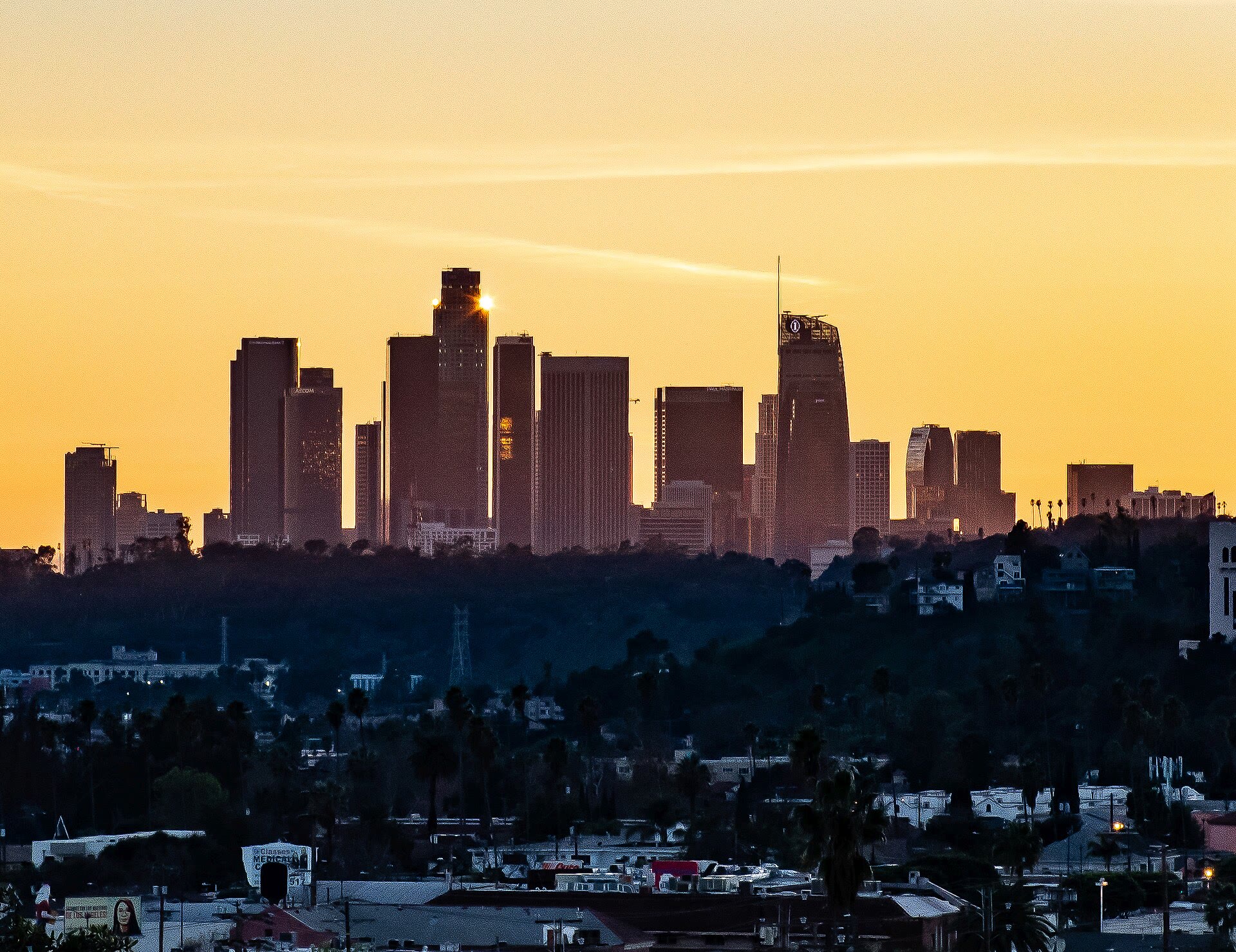 Downtown Los Angeles glowing at sunset beyond the rooftops of Highland Park