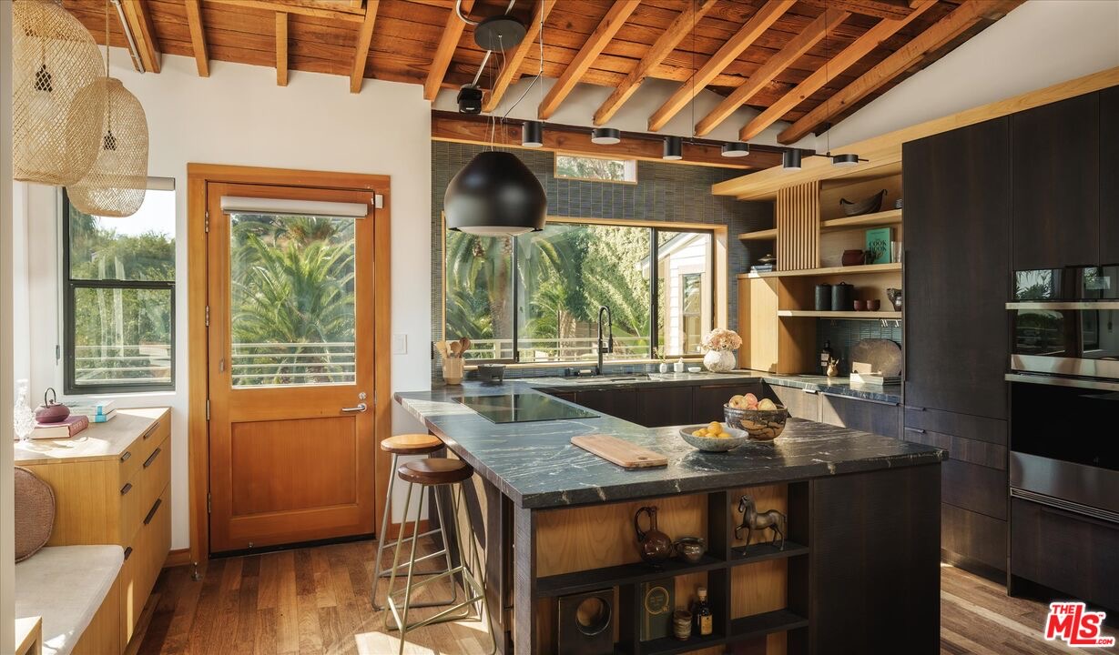 Dark kitchen with near-black cabinetry, stone counters, exposed beams, and skylights at 1811 Micheltorena Street