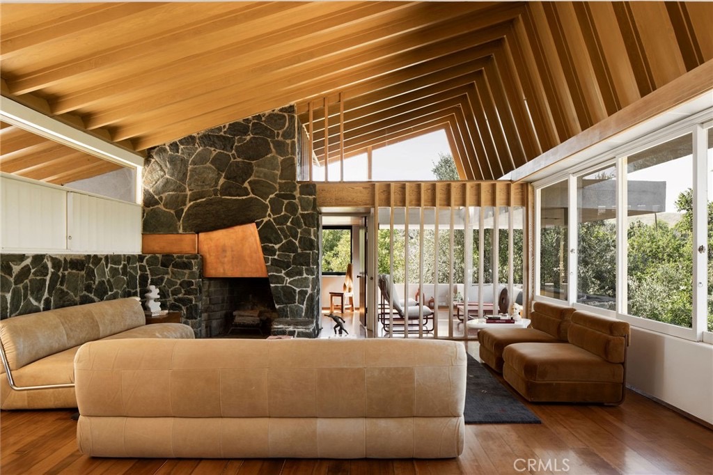 Double-height great room with angled wood beams, clerestory glass, stacked stone, and a copper fireplace hood
