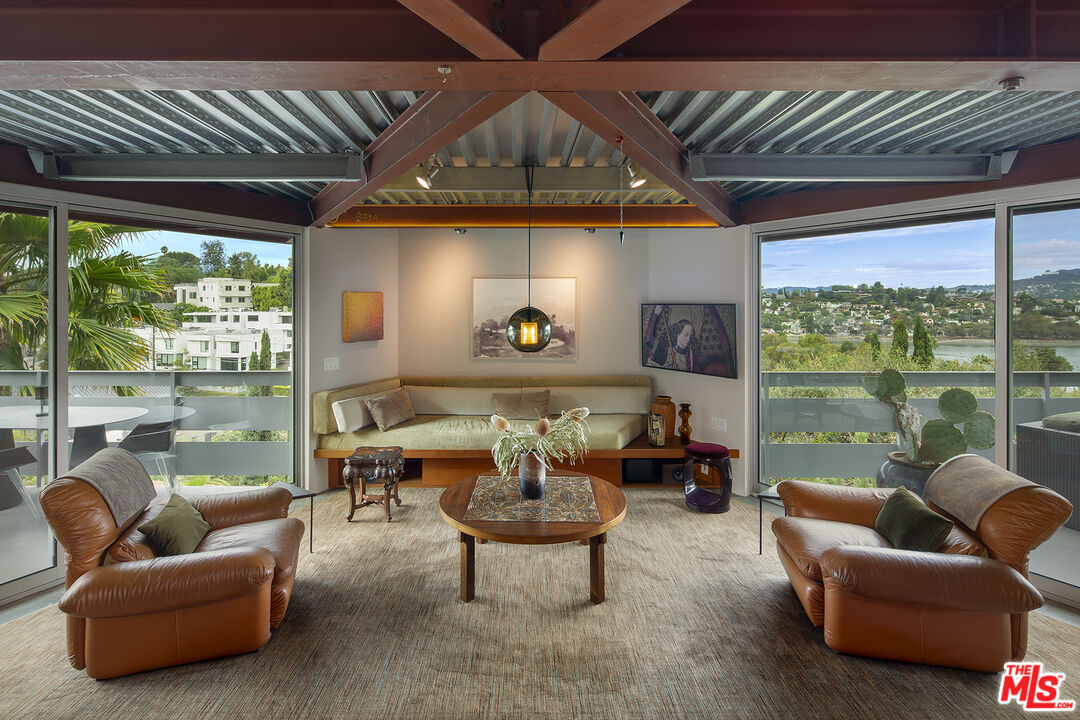 Living room with crossed structural beams and glass walls framing the Silver Lake reservoir on both sides at 2383 Loma Vista Pl