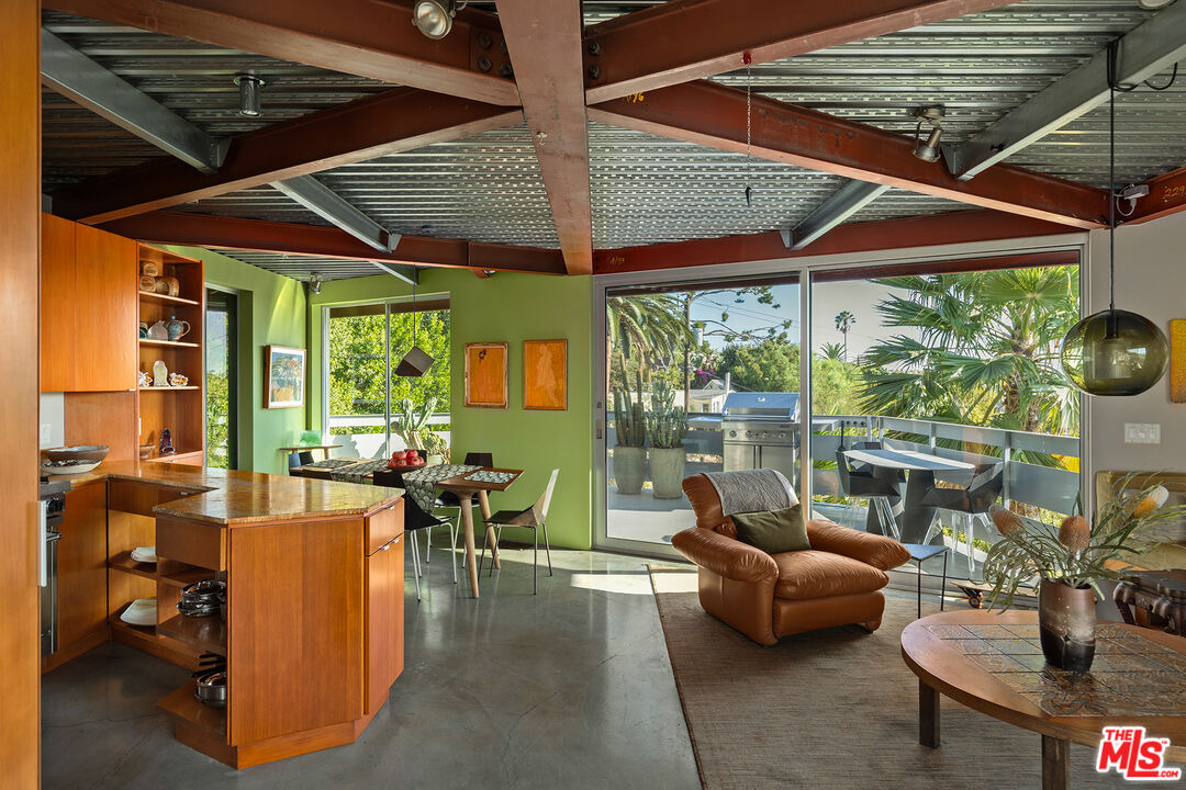 Kitchen and built-in desk under angled steel beams opening to the palm-shaded deck at 2383 Loma Vista Pl