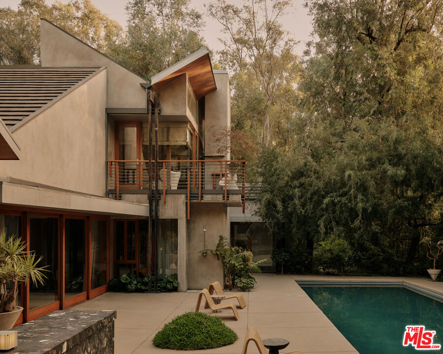 Wood-and-concrete modern home beside a pool and mature trees at 7728 Woodrow Wilson Dr