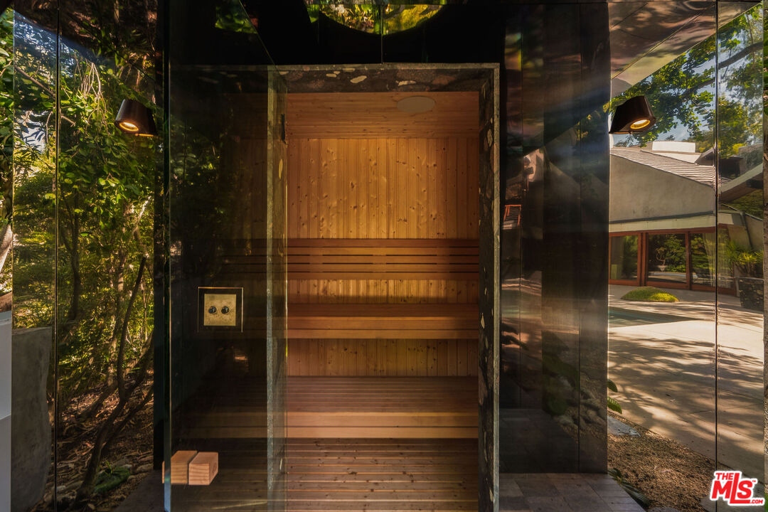Cedar sauna set inside a mirrored garden structure reflecting the trees and house at 7728 Woodrow Wilson Dr