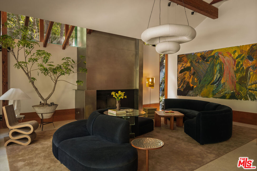 Living room with sculptural seating, exposed timber beams, abstract art, and a metal fireplace at 7728 Woodrow Wilson Dr