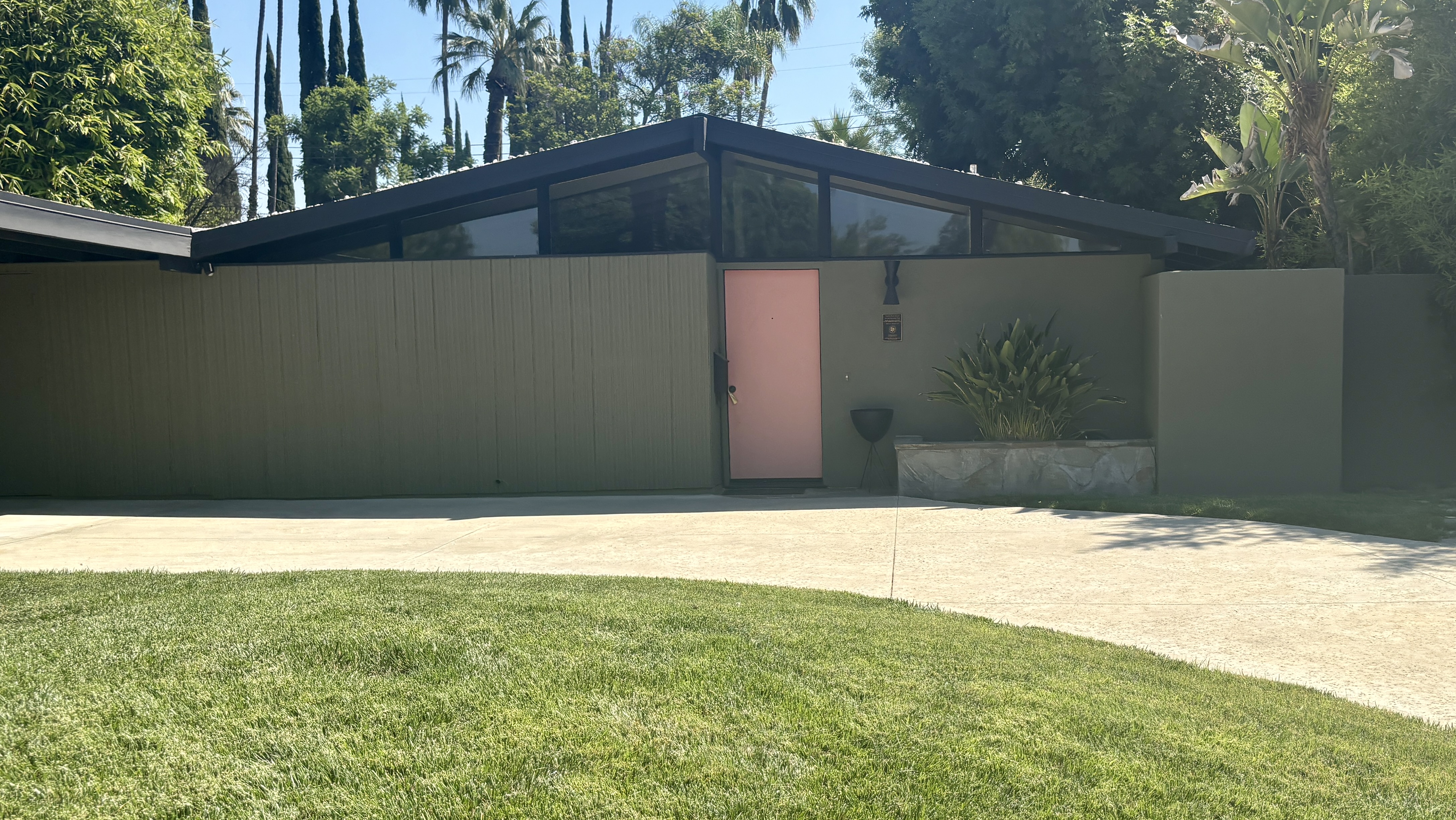 Olive-green 1954 Palmer and Krisel home with a pink door in the Corbin Palms tract